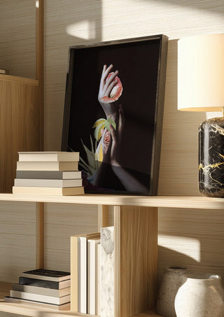 Hypnopompic by Rocio Montoya in a dark frame on a wooden shelf beside books and a lamp