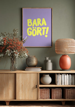 Bara gört! by Grafik bageri above a wooden sideboard on a sage green wall
