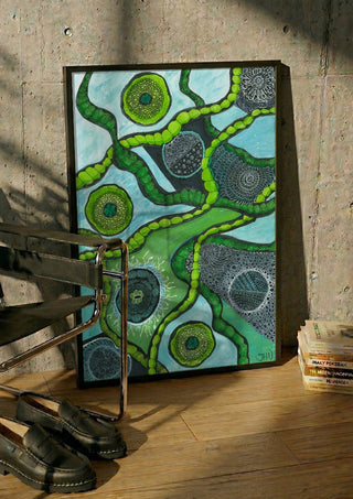 Green Cells by JHN.ByHjort in a black frame leaning against a concrete wall by a steel chair