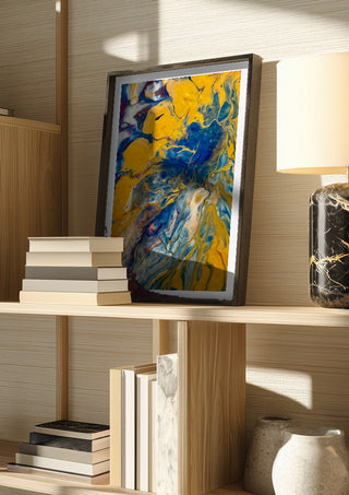 Gold and Indigo by Da Winters in a dark frame on a wooden shelf beside books and a lamp