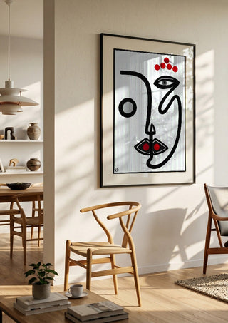 Face by RA in a black frame in a bright dining room with wooden chairs