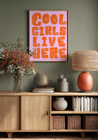 Cool girls live here by Ohkimiko above a wooden sideboard on a sage green wall