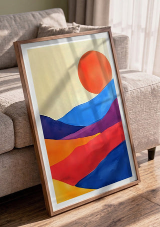 Red sun over colourful hills by Ohkimiko in a walnut frame leaning against a grey sofa