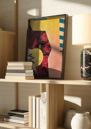 Roses by Kareem Rizk in a dark frame on a wooden shelf beside books and a lamp