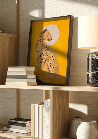 Leopard by ThingDesign in a dark frame on a wooden shelf beside books and a lamp
