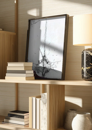 Ship and Gulls by Justyna Kopania in a dark frame on a wooden shelf beside books and a lamp