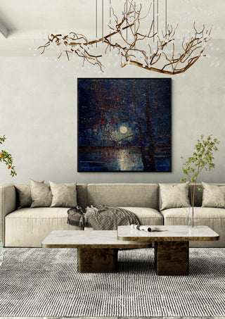 Moon through Bare Trees by Justyna Kopania in a black frame above a cream sofa under a branch chandelier