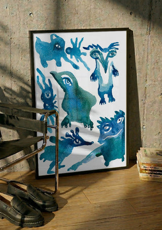 Creatures by Lena Galé in a black frame leaning against a concrete wall by a steel chair