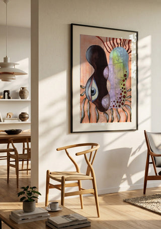 Two Heads, One Eye by Shimmering Ugly in a black frame in a bright dining room with wooden chairs