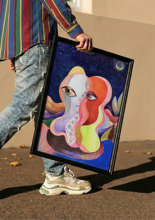 Two Faces Under the Moon by Shimmering Ugly carried in a black frame along a sunny street