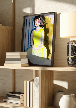 Yellow Dress by DNF in a dark frame on a wooden shelf beside books and a lamp