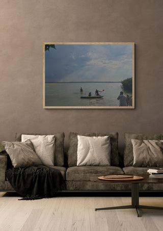 The Lake’s Shared Rhythm by Bora Kőhalmi in a light oak frame on a warm grey wall above a brown sofa