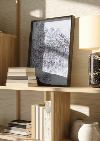 Nike by Priit Ruttas in a dark frame on a wooden shelf beside books and a lamp