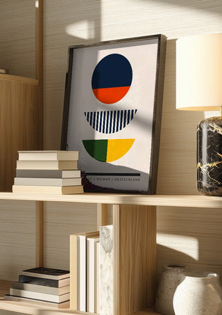Bauhaus Circles by Neil Stevens in a dark frame on a wooden shelf beside books and a lamp