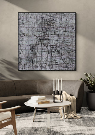 looks like a house by Priit Ruttas in a black frame above a dark grey sofa with a round table and candlesticks