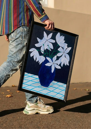 Blå blomster på rutig duk by Rebecka Hansson carried in a black frame along a sunny street