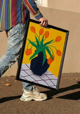 Orangea blomster i brun vas by Rebecka Hansson carried in a black frame along a sunny street