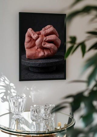 Hold Me - Terracotta Hands by Ammar in a black frame above a glass table with crystal glassware
