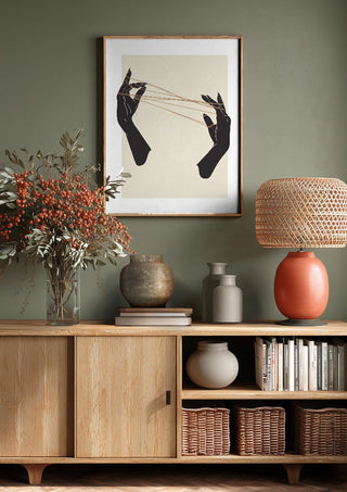 Unclear plans by Nari above a wooden sideboard on a sage green wall