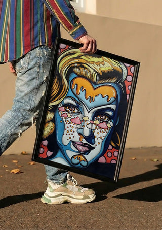 Marylin Monroe by Okiana carried in a black frame along a sunny street