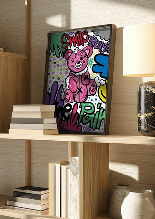 Smile Through The Pain by Bibi in a dark frame on a wooden shelf beside books and a lamp