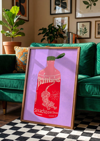 Sriracha chili sauce by Astrid Lind in a wooden frame beside a green velvet sofa on a chequered floor