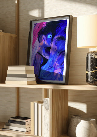 Embrace by Vanyay in a dark frame on a wooden shelf beside books and a lamp