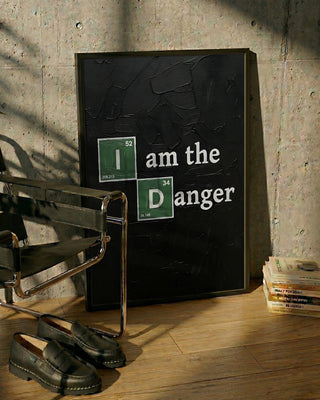 Framed "I am the Danger" poster with science theme, leaning against a wall beside a chair and books.