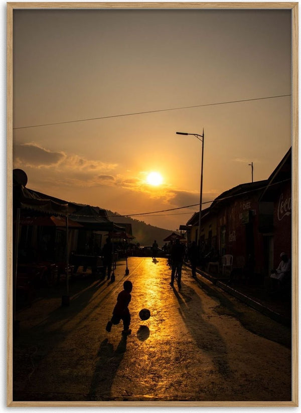 Soccer on the street by Gloria Mwivanda - a boy with a ball silhouetted on a golden street at sunset